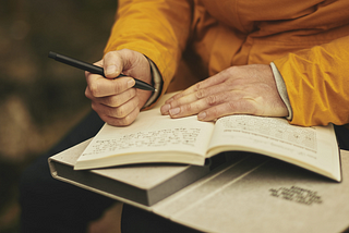 A person holds a journal in their lap, pen poised to continue writing an entry scrawled across the page.