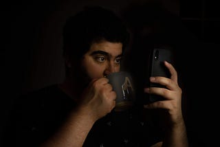 Holding phone while sipping tea, blacked out background