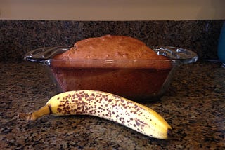 A picture of banana bread and a spotted banana on a counter top.