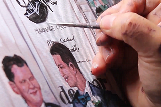 Detail up close of a painting of two grooms. Hand with brush on the right.