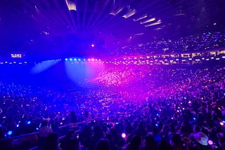 An arena full of people with blue and pink lighting mixed in halves