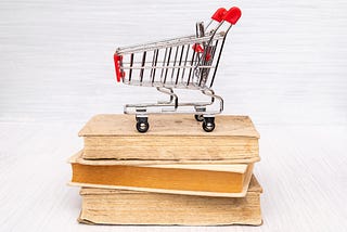 A mini shopping cart sitting on top of a stack of three books