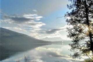 Serene lake, mountain, tree, and many beautiful clouds creating a mirror-like effect. An as above so below feeling.