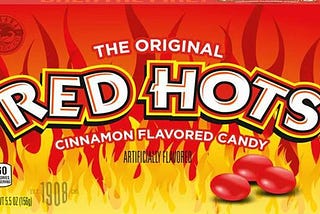 Movie theater-style box of Red Hots candy, reading “The Original Red Hots Cinnamon Flavored Candy,” with several candies against a background of cartoon flames.