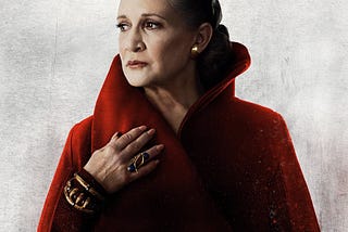 Image description: General Leia Organa looking off to the right and looking regal in a high-collared red cape. End ID