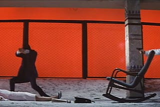 Tetsu firing a gun at a man while a woman lies dead on the ground.