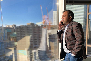 Photo of Minister Rasheed looking out to downtown Toronto from the main offices of the Ontario Digital Service while taking a stakeholder call.