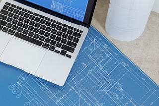 MacBook with an image of a blueprint of some part on top of the table with the same blueprint, but printed out