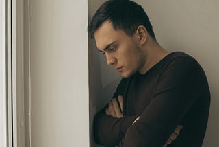Slightly filtered image of a man standing next to a window looking down.