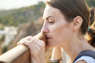 A brown haired woman looking out onto something. Her face resting against a brown plank of wood.