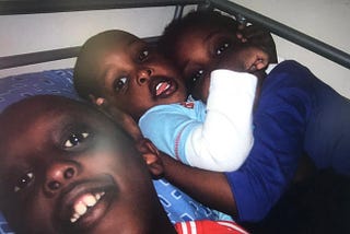 photograph of 3 black kids next to each other on a bed look into the camera