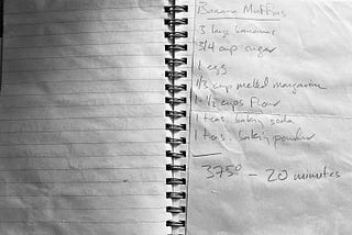 a black and white photo of a handwritten recipe for banana muffins on a worn page of a spiral notebook