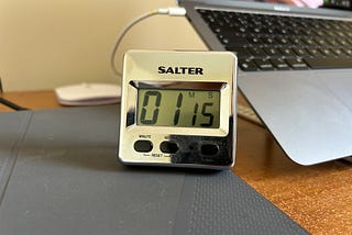 A timer made by Salter showing time being counted and has reached 1 minute 15 seconds. Behind it stands a laptop tilted on a stand. Image: Roland Millward