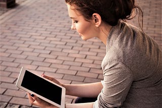 girl with brown hair gathered up on her head wearing light tan shirt and holding tablet