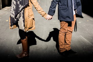 Couple wearing fall coats and boats holding hands on street