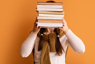 A woman holding a stack of books in front of her face.