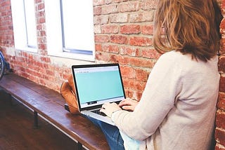 An image of a woman working on a laptop on a bench