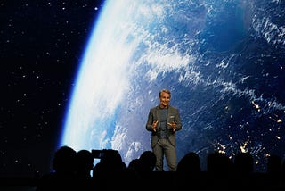 Peter Körte, Siemens’ Chief Technology and Strategy Officer, posed during his keynote at CES 2025. A picture of planet earth is behind Peter wo wers a grey suit.