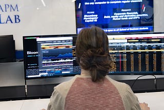 A girl sits in front two computer monitors while navigating the Bloomberg Terminal.