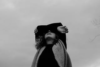 A black and white photo of a girl standing and looking up, closing her eyes with her arms