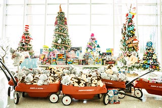 5 holiday trees with wagons full of gifts and toys in the foreground