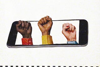 A smart phone lays on its side. Rising up from the screen are three human fists, symbolizing power and resistance. One fist is dark-skinned Black and wearing red. The other fist is lighter-skinned Black, or possibly Brown, and wearing yellow. The third fist is white and slightly smaller. The nails on this one are painted red and they are wearing blue.