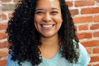 Kamila smiling in front of a brick wall