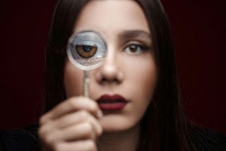 Woman with long dark hair holding a magnifying glass to her eye, to magnify it.