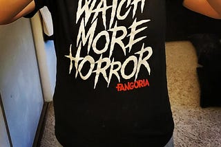 Black t-shirt with the phrase “Watch More Horror” in white font and “Fangoria” in red font.