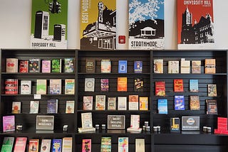 Dark bookshelves full of books displayed face out underneath four colorful works of art.