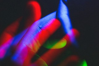 Hands intertwined, bathed in neon lights in blue, green, and red against a dark background