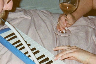 A couple plays a melodica together while drinking wine.