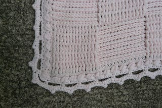 A pink crochet blanket worked in a textured basketweave stitch