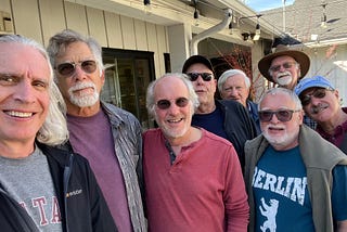 8 older men, white-haired or balding, standing outside