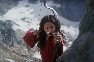 Mulan, from the live-action 2020 movie, is standing with her bow and arrow, ready to fire at the enemy.