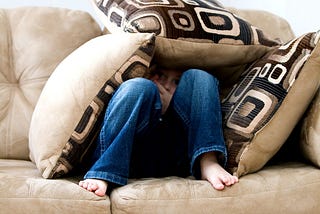 a person huddled under pillows on a sofa