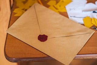A lettter sealed in a brown envelope with a wax seal sits on a wooden desk