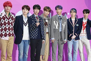 Seven humans standing side by side dressed trendy at an awards show