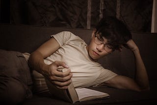 Thoughtful Asian young man reading book on couch