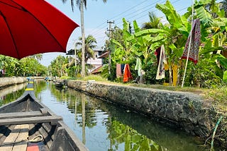 A boat is shown in a narrow canal, lined with banana and coconut trees