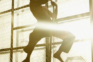 Fit barefoot man using only arm strength to pull himself up a rope in a gym