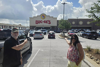 Two travelers stand outside a Buc-ee’s travel center in Texas, pointing toward the famous store that has become a surprising attraction for international visitors exploring America during the World Cup.