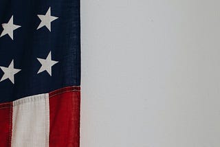 A segment of an American flag hanging veritcally on a white wall.