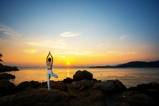 A woman practices yoga on a cliff at sunset