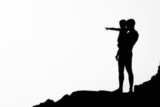 Black and white silhouette image, man holding child pointing to horizon.