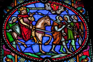 Stained glass window showing a warrior on horseback with your others on foot under a cross as they march to Jerusalem in the first Crusade.