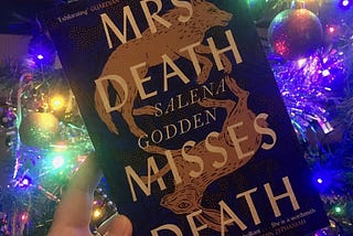 Photograph of the book, Mrs Death Misses Death by Salena Godden. There is a colourfully lit Christmas tree in the background.