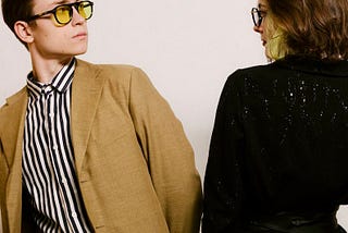 Two people in blazers and glasses staring each other down