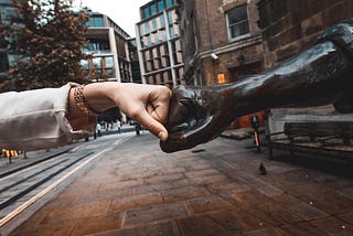 Uma mão cumprimentando uma estátua com “socos”