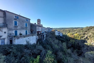 A stone village in france with a church tower. It sits on a hill overlooking a green valley.